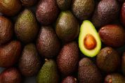 Viele reife grün-braune Avocados und eine halbierte mit Kern Viele reife grün-braune Avocados und eine halbierte mit Kern